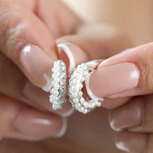 Model Holding Hoops Model Holding Crystal and Pearl Huggie Hoop Earrings in Silver Between Fingers