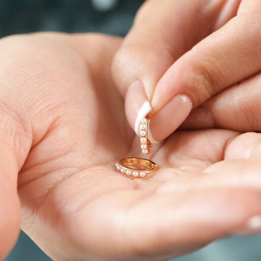 Model Holding Pearl Studded Huggie Hoop Earrings in Gold in Between Fingers