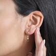 Close Up of Stone and Pearl Drop Huggie Hoop Earrings in Gold on Model with Hand Behind Ear