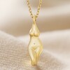 Close Up of Feminine Figure Pendant Necklace in Gold on Beige Material
