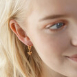 Close Up of Mismatched Daisy and Bee Huggie Hoop Earrings in Gold on Model