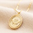 Close up of Bee Oval Disc Pendant Necklace in Gold on beige fabric