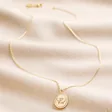 Close up of Bee Oval Disc Pendant Necklace in Gold on beige fabric