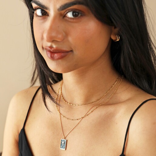Dark Haired Model Looking at Camera Wearing Enamel Blue Moon Tarot Card Pendant Necklace in Gold
