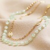 Close Up of Set of 2 Leaf Chain and Beaded Necklace in Gold on Beige Fabric