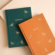 Personalised Bee Fabric Notebooks in orange and teal on plain surface