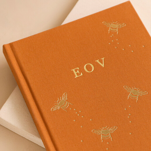 Close up of debossed initials on the Personalised Initials Bee Fabric Notebook on plain pink surface