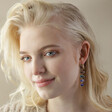 Model Looking to Side Wearing Big Metal London Blue Stone Luxe Drop Earrings in Gold