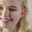 Close Up of Model Smiling Wearing Big Metal London Blue Stone Luxe Drop Earrings in Gold