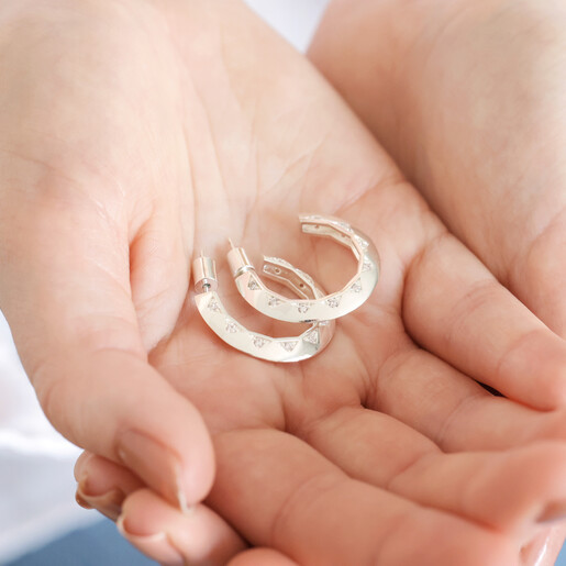 Model Holding Estella Bartlett Geometric Crystal Hoop Earrings in Silver in Palm of Hand