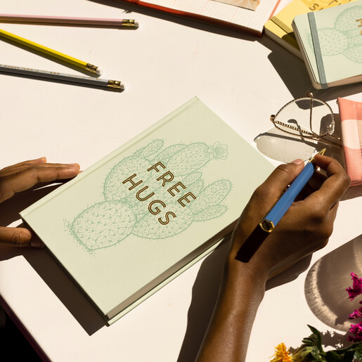 Model using the Designworks Inks Free Hugs Lined Notebook on desk with pen