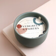Paddywax Evergreen and Embers Scented Candle with dust cover on top of wax on neutral coloured background