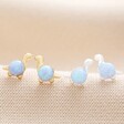 Blue Opal Dinosaur Stud Earrings in Gold on Beige Fabric with Silver Version