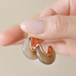 Model Holding Cocoa Organic Resin Hoop Earrings in Gold Between Fingers