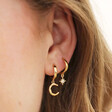 Close Up of Crescent Moon & Star Charm Huggie Hoop Earrings in Gold on Model