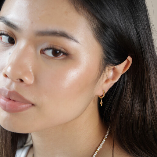 Model Looking to Side Wearing Lightning Charm Mismatched Star and Lightning Huggie Hoop Earrings in Gold