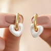 Model Holding Pearl Resin Heart Huggie Hoop Earrings in Gold in Front