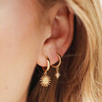 Close Up of Model Wearing Sunburst and Star Charm Huggie Hoop Earrings in Gold