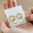 Model Holding Crystal Flower and Enamel Bee Stud Earrings in Gold in Packaging