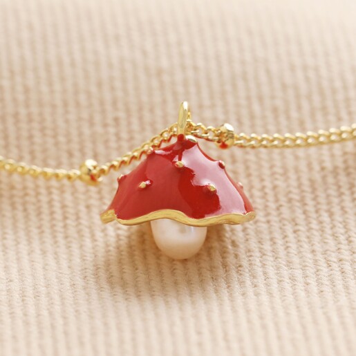 Close Up of Pearl and Enamel Toadstool Anklet in Gold on beige ribbed fabric