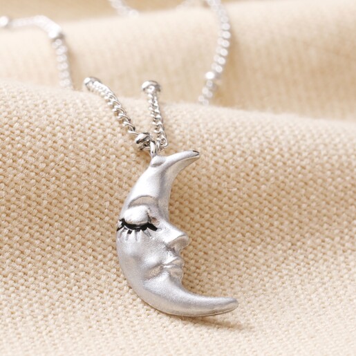 Close Up of Sleeping Moon Pendant Necklace in Silver on Beige Fabric