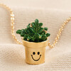 Close up of Smiley Planter Pendant Necklace in Gold on beige fabric