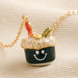 Close up of Smiley Sushi Pendant Necklace in Gold on beige fabric