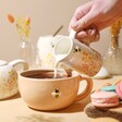 Model Pouring Milk From Jug Into Mug From Dusky Pink Floral Ceramic Teapot and Mug Set