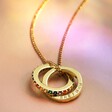 Gold Personalised Rainbow Pride Eternity Pendant Necklace on beige fabric in rainbow lighting