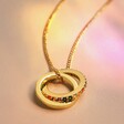 Rainbow Pride Eternity Pendant Necklace in Gold on beige fabric in rainbow light