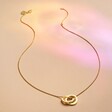 Full length Rainbow Pride Eternity Pendant Necklace in Gold on beige fabric in rainbow light