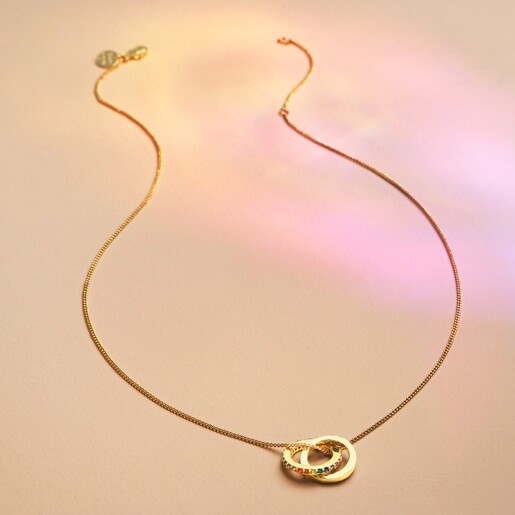 Full length Rainbow Pride Eternity Pendant Necklace in Gold on beige fabric in rainbow light