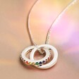 Rainbow Pride Eternity Pendant Necklace in Silver on beige fabric in rainbow light