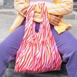 Model in purple trousers using the pink and red Kind Bag Wild Stripes Reusable Shopping Bag