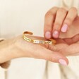 Model holding Adjustable 'Sisters' Meaningful Word Wave Bangle in Gold in palm of hand