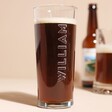 Personalised Bold Name Pint Glass Filled with Beer with Beer Bottle and Other Glass in Background