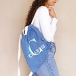 Model wearing Personalised Initial Name BagBase Denim Drawstring Bag on back in front of neutral backdrop