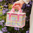 Sass & Belle Danish Pastel Lunch Bag in Hand with Purple Flowers and Green Leaves Background