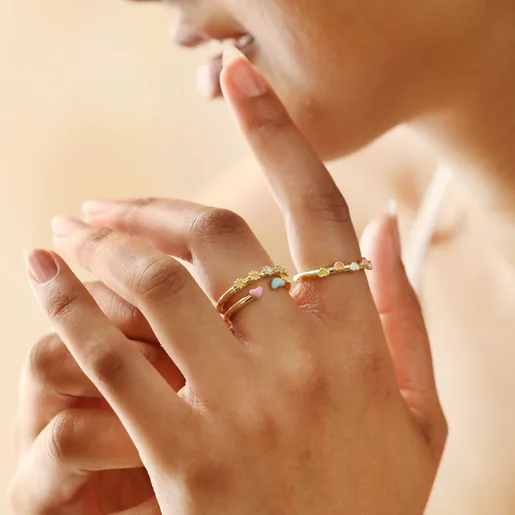 Model Wears Adjustable Enamel Heart Ring in Gold Stacked With Other Gold Rings