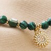 Close Up of Green Semi-Precious Beaded Bracelet with Sun Charm in Gold on Beige Fabric