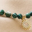 Close Up of Green Semi-Precious Beaded Bracelet with Sun Charm in Gold on Beige Fabric