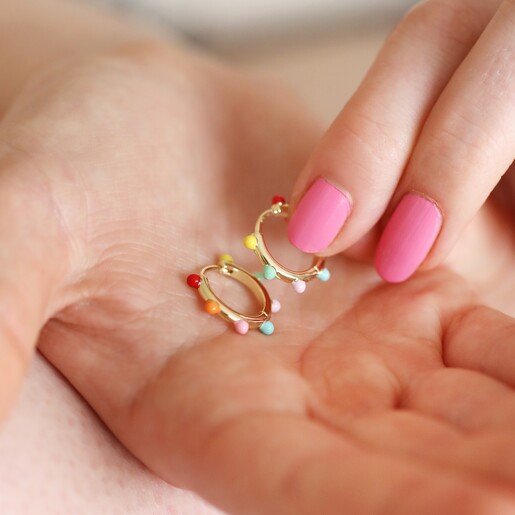 Model holding the Colourful Enamel Pom Pom Huggie Hoop Earrings in Gold in hands