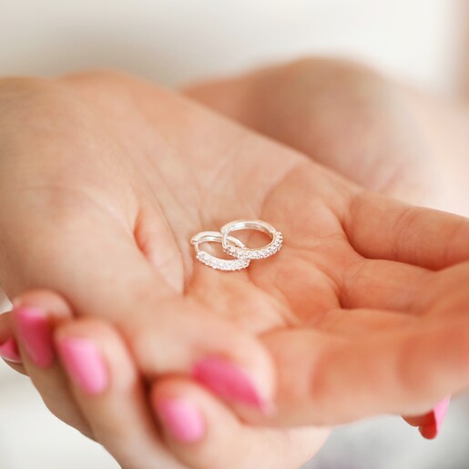Crystal Huggie Hoops in Silver held in models hands