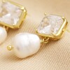 Close up of Crystal Stud and Freshwater Pearl Drop Earrings in Gold on beige fabric