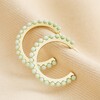 Green Stone Hoop Earrings in Gold on Neutral Coloured Fabric 