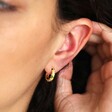 Close up of Mustard Cloisonné Huggie Hoop Earrings in Gold on model with hand behind ear