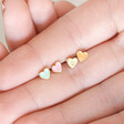 Model holding Set of 4 Mismatched Heart Face Stud Earrings in Gold in between fingers