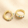 Blue Stone and Pearl Huggie Hoop Earrings in Gold on top of beige coloured fabric