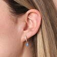 Close up of Blue Teardrop Crystal Huggie Hoop Earrings in Silver on model