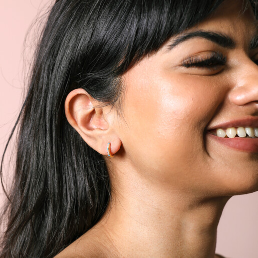 Blue Stone and Pearl Huggie Hoop Earrings in Gold on model smiling against beige coloured backdrop